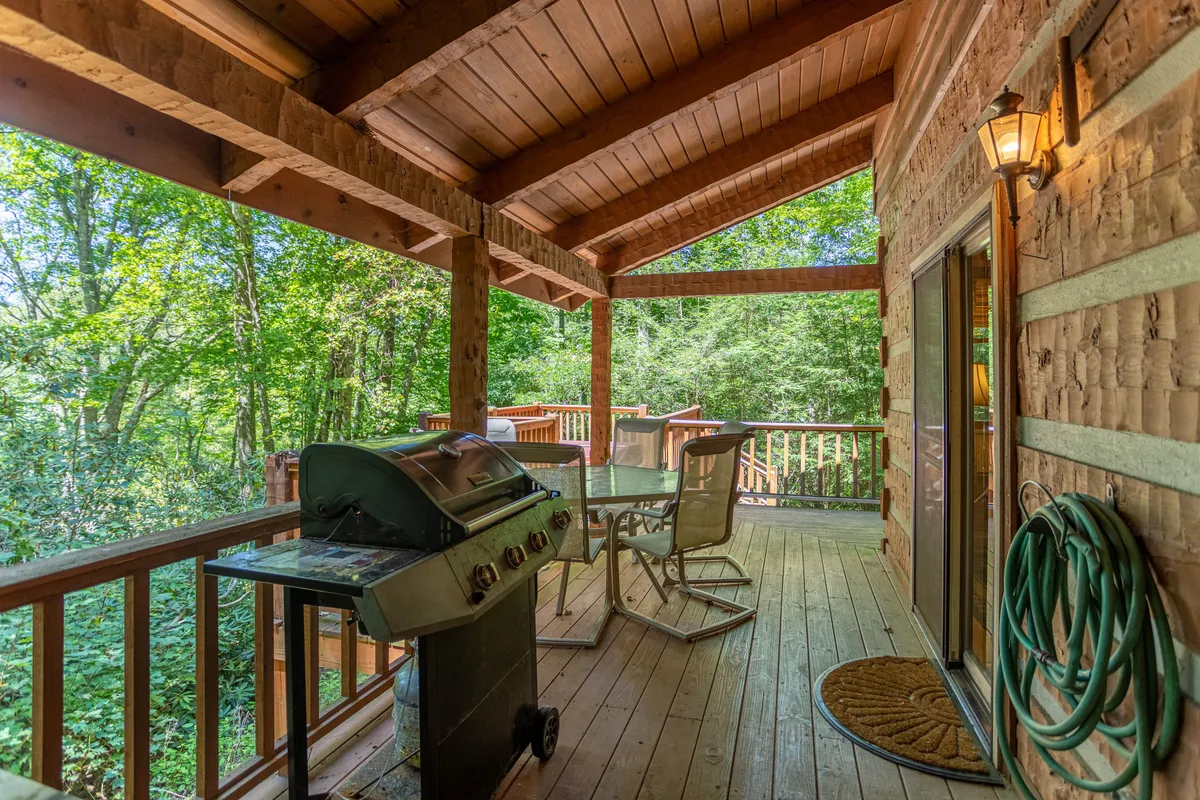 A close-up view of the outdoor grill and dining table, bordered by a wooden railing and lush foliage. The scene is inviting for barbecues, family celebrations, and morning coffee in a serene, natural setting.