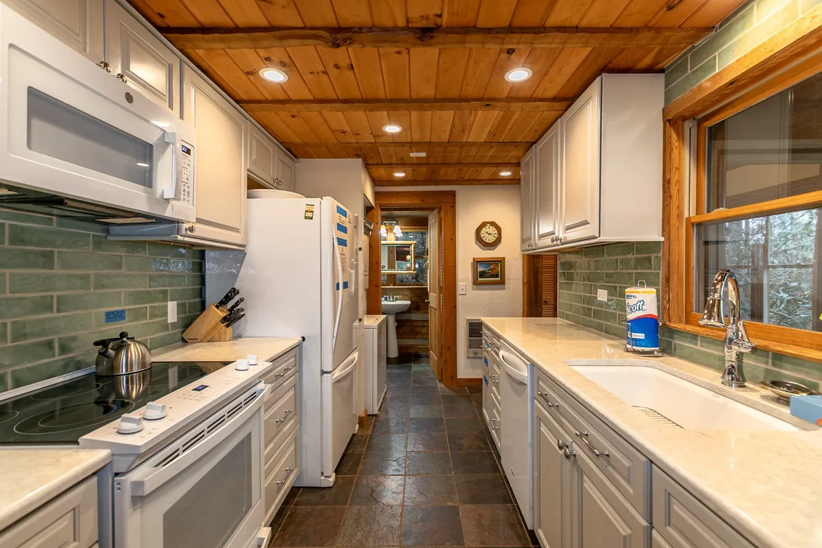 A cozy mountain kitchen with modern appliances, a green backsplash, and rustic wooden ceilings. The scene is inviting and clearly designed for both meal prep and gathering, with space to connect while cooking.