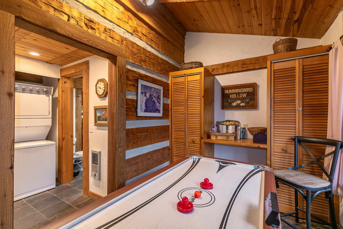 A playful interior with log walls and a central air hockey table, surrounded by cozy storage cabinets and a decorative sign. The space is designed for friendly competition and laughter during rainy days or evening gatherings.