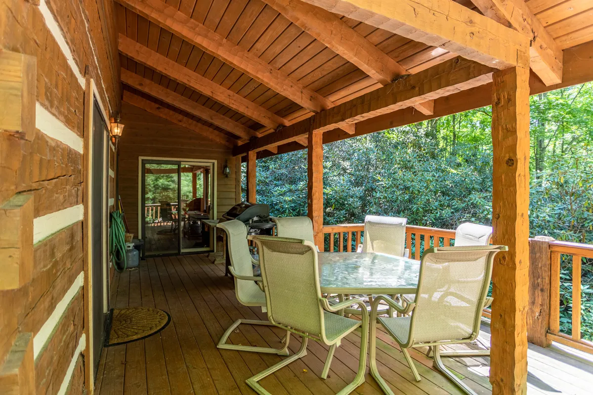 A spacious wooden deck set against lush greenery, featuring an outdoor dining table and grill—perfect for family meals and gatherings in the fresh mountain air. The view suggests an expansive yard and direct access to the outdoors, highlighting the home's connection to nature and space for outdoor fun.