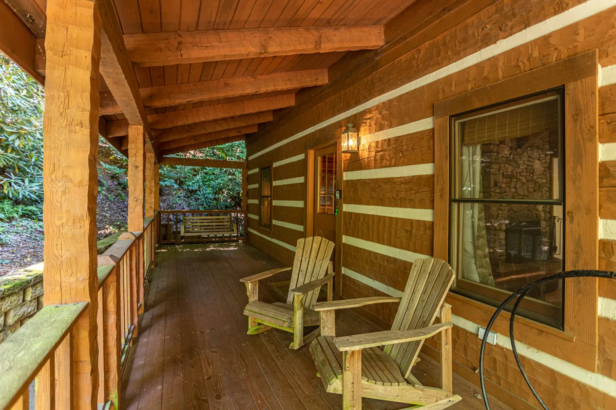 A cozy log cabin nestled among lush greenery with classic wooden rocking chairs on the porch, offering a peaceful outdoor space for relaxation or enjoying the surrounding nature.