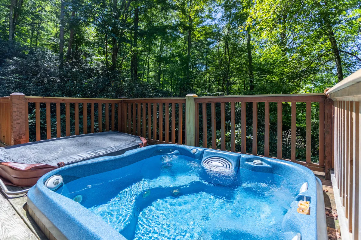 A bubbling outdoor hot tub sits on the deck, framed by lush greenery and the sturdy railing. The hot tub offers a front-row seat to the tranquil outdoors, inviting guests to unwind while immersed in natural beauty.