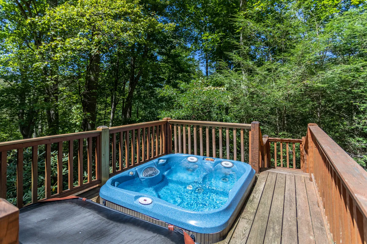 A serene wooden deck with a private hot tub, surrounded by vibrant greenery, offering a tranquil spot for couples to unwind and connect with nature.